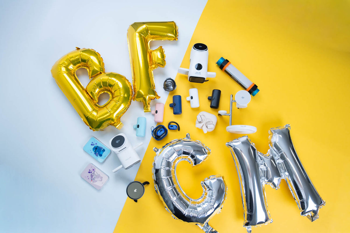 Gold BF and silver CM balloons on a blue and yellow background, surrounded by PTC power banks, wireless chargers and earbuds