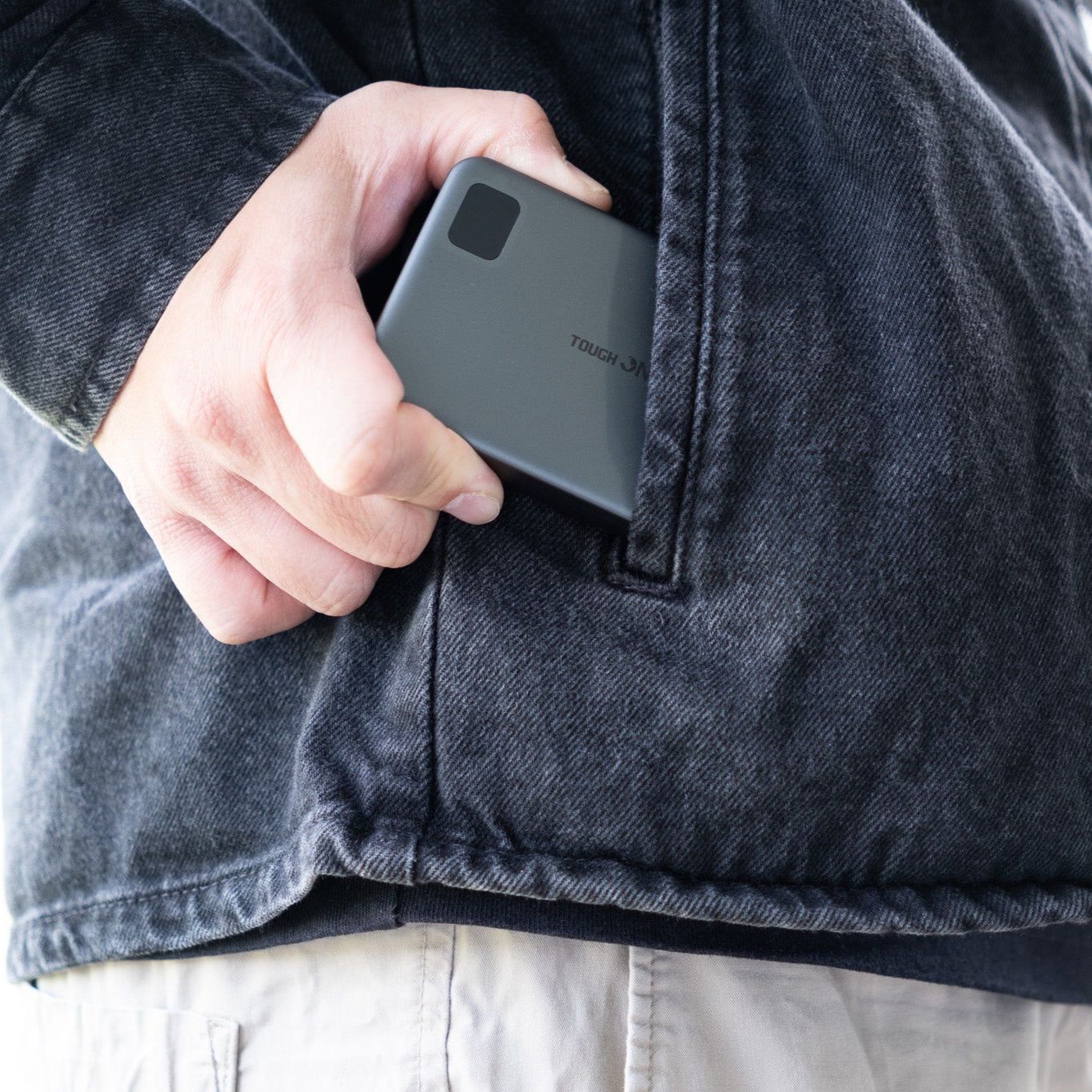 Person holding a slim power bank with a visible brand logo, wearing a dark denim jacket.