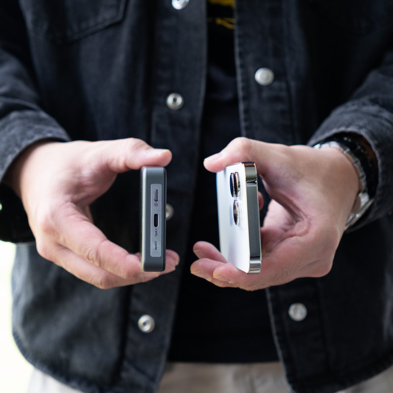 Person holding two electronic devices in their hands, wearing a dark jacket.