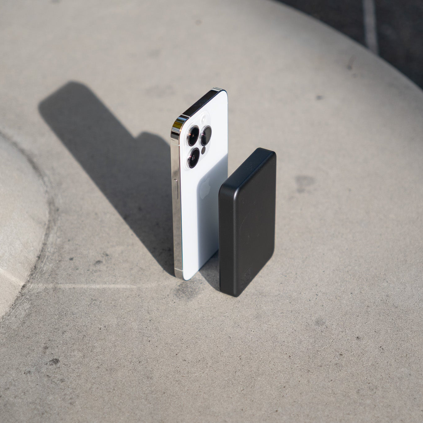 Two smartphone cases, one black and one silver, on a concrete surface.