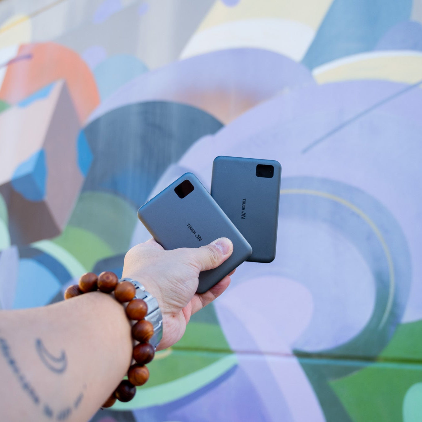 Person holding two ultra slim power banks in front of a colourful mural