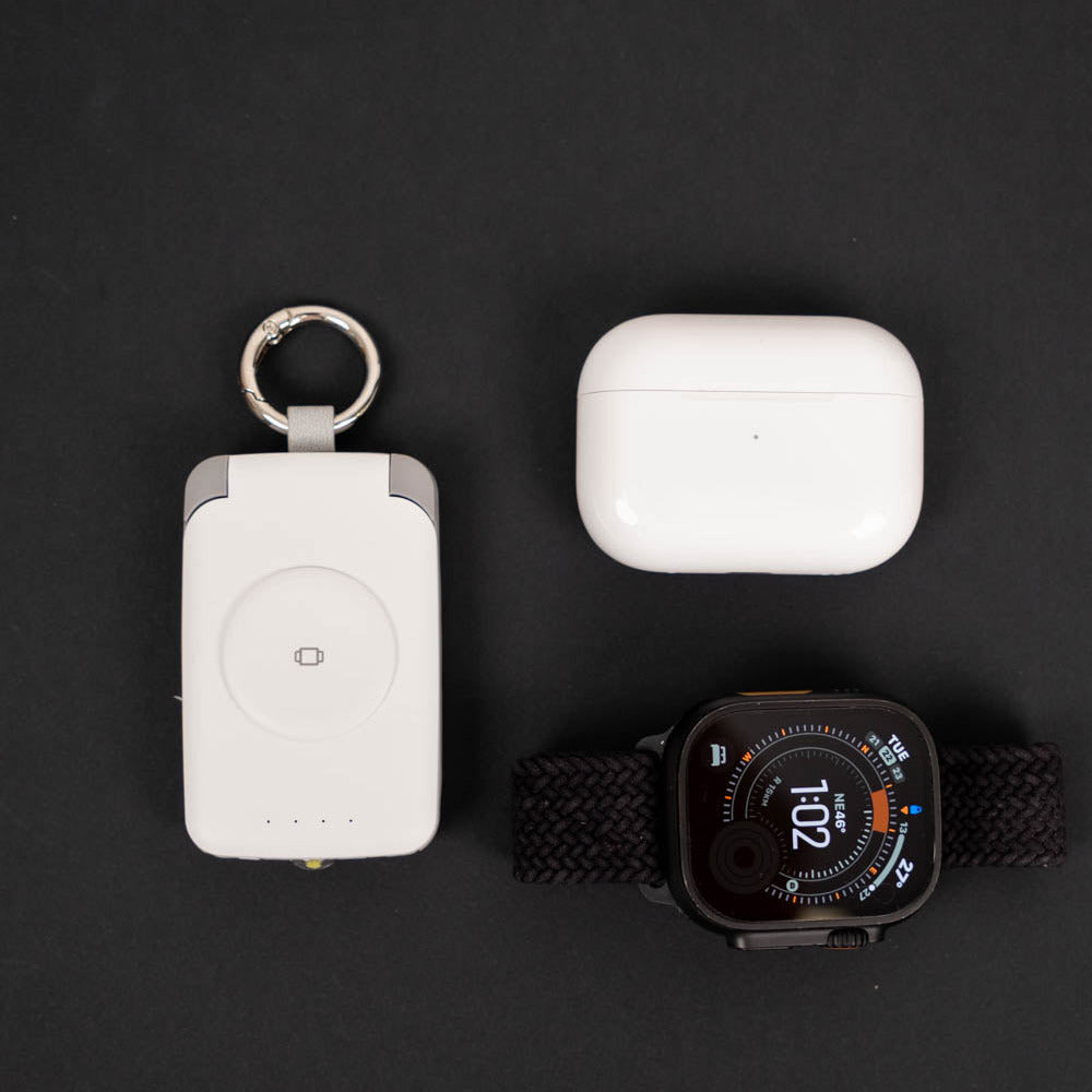 Top-down view of a white PTC WatchGo 2000 beside AirPods Pro and an Apple Watch Ultra