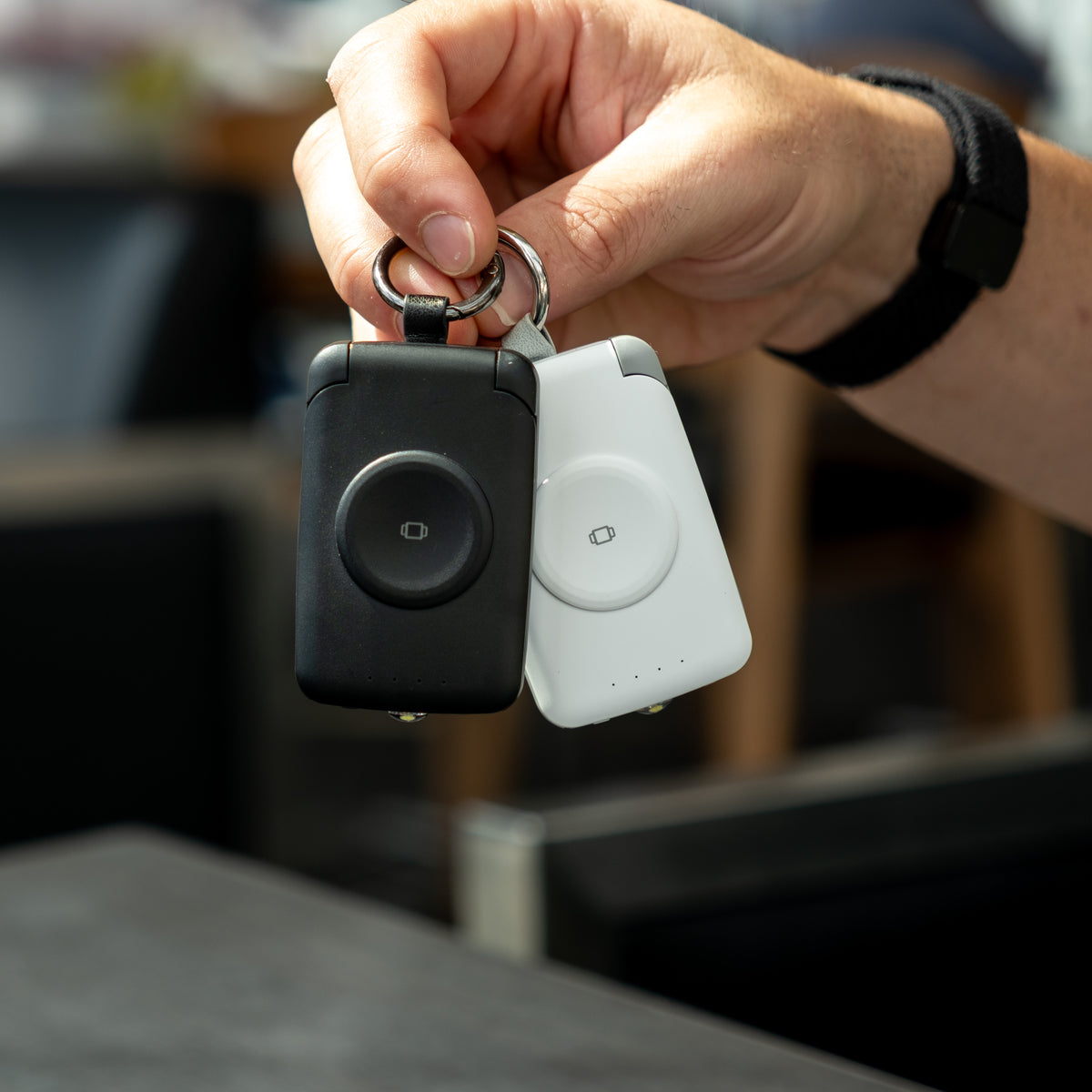 Hand holding a black and a white PTC WatchGo 2000 power bank by their keyrings