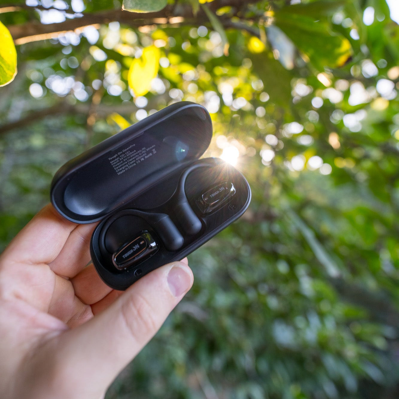 Person holding a open-ear wireless headphones in front of the bush