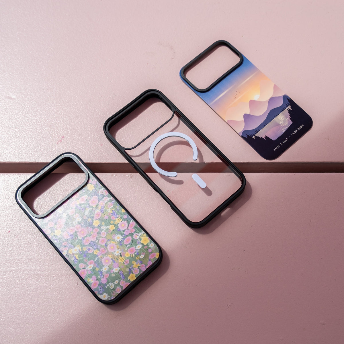 Custom skin MagSafe iPhone cases spread on a pink surface, showing the clear MagSafe case beside two printed skins
