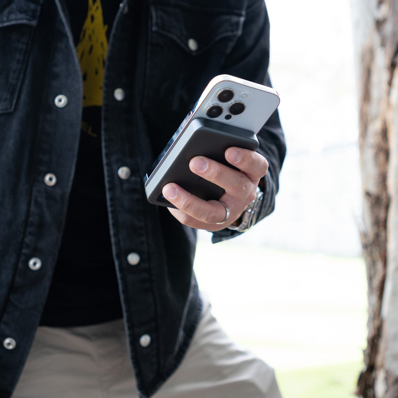 Person holding a smartphone with slim power bank next to a tree