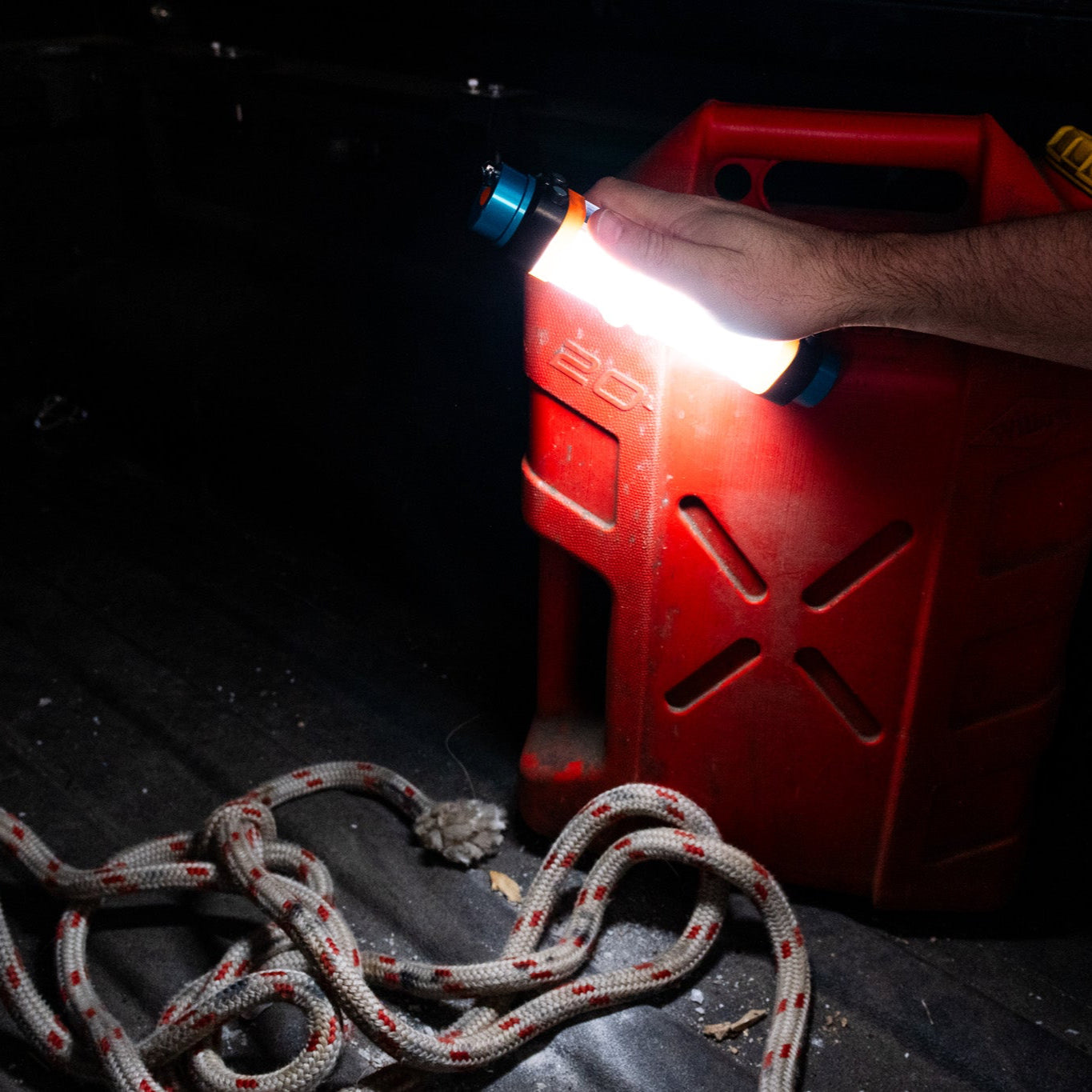 Person using a flashlight on a red gas canister in a dark setting