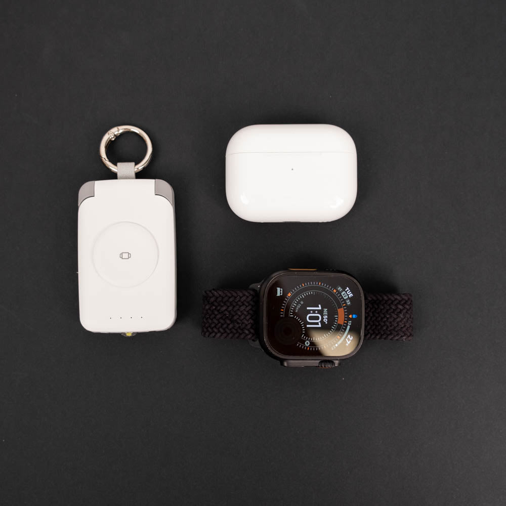 White PTC WatchGo 2000 laid out with AirPods Pro and an Apple Watch Ultra on black