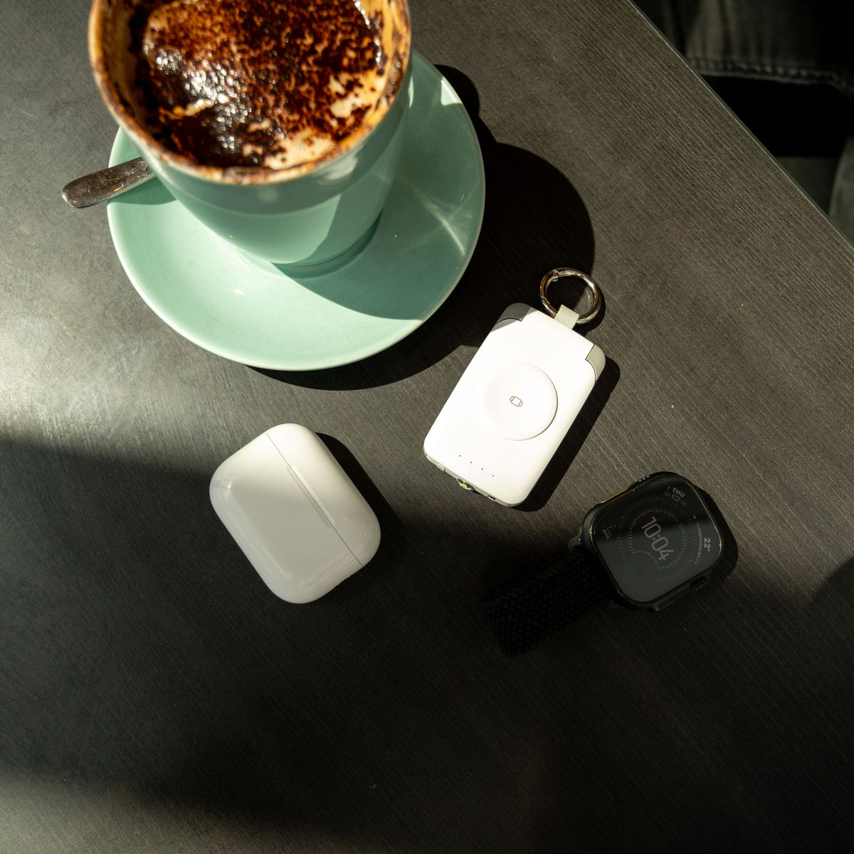 Black and white PTC WatchGo 2000 power banks on a cafe table with AirPods and a coffee