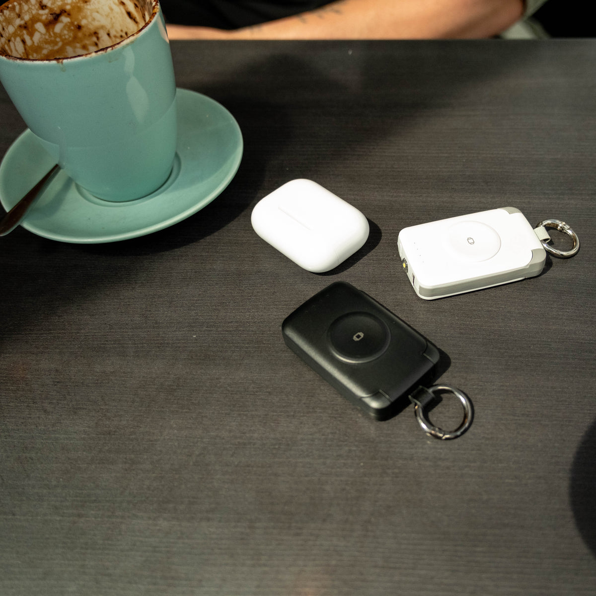 Black and white PTC WatchGo 2000 power banks beside AirPods on a cafe table