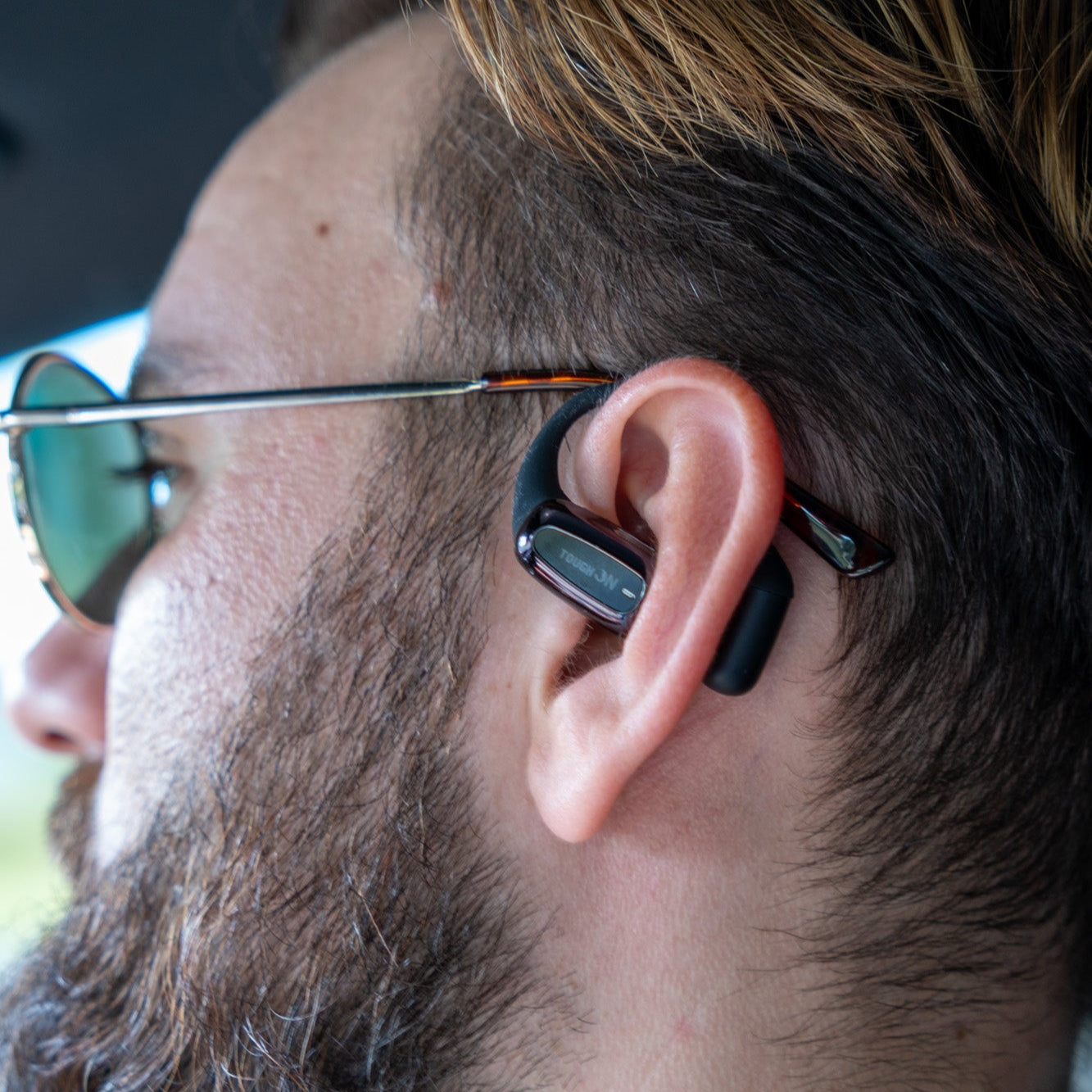 Person wearing a black wireless earbud with sunglasses on.