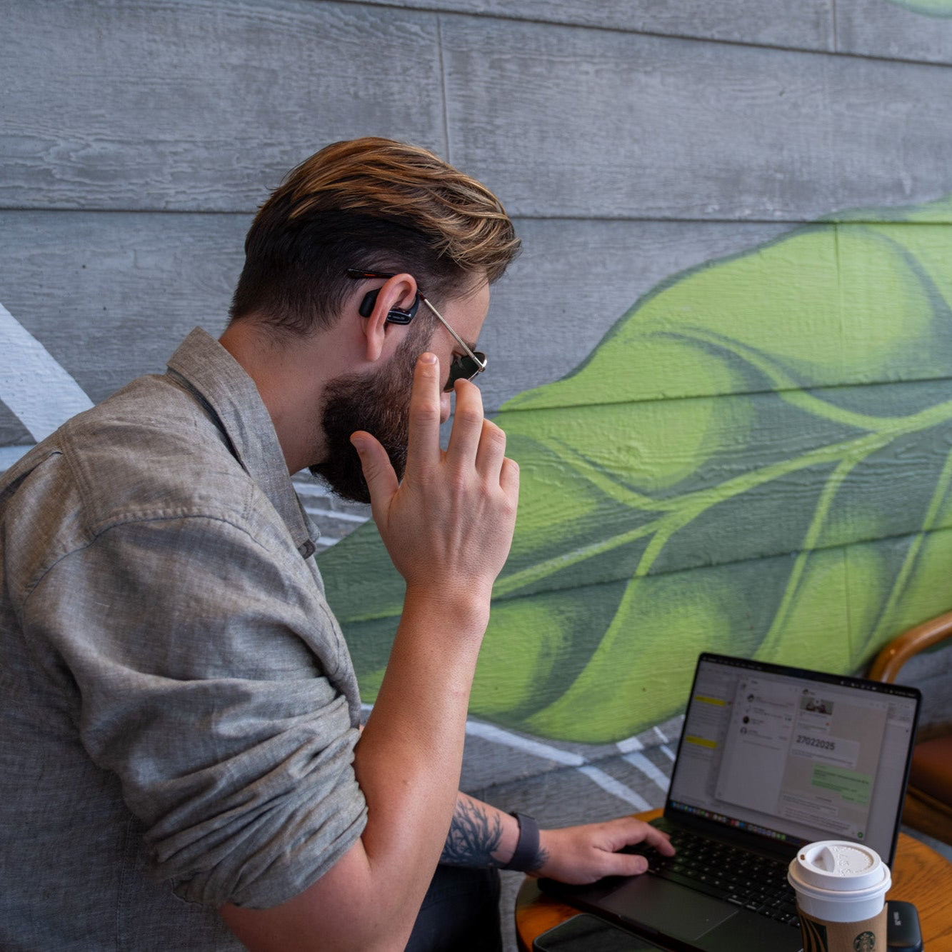 Person answering phone call with open-ear wireless headphone in coffee shop